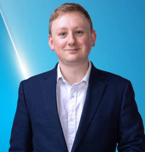 Sam Boswell, wearing a navy blue suit and white shirt, smiling at the camera against a blue background. Text reads: 'Sam Boswell’s Aintree Day Two Tips' with '18+ Gambleaware.org' at the bottom.